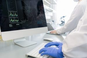 Horizontal shot of two unrecognizable scientists wearing white coats gloves working in laboratory using modern computers